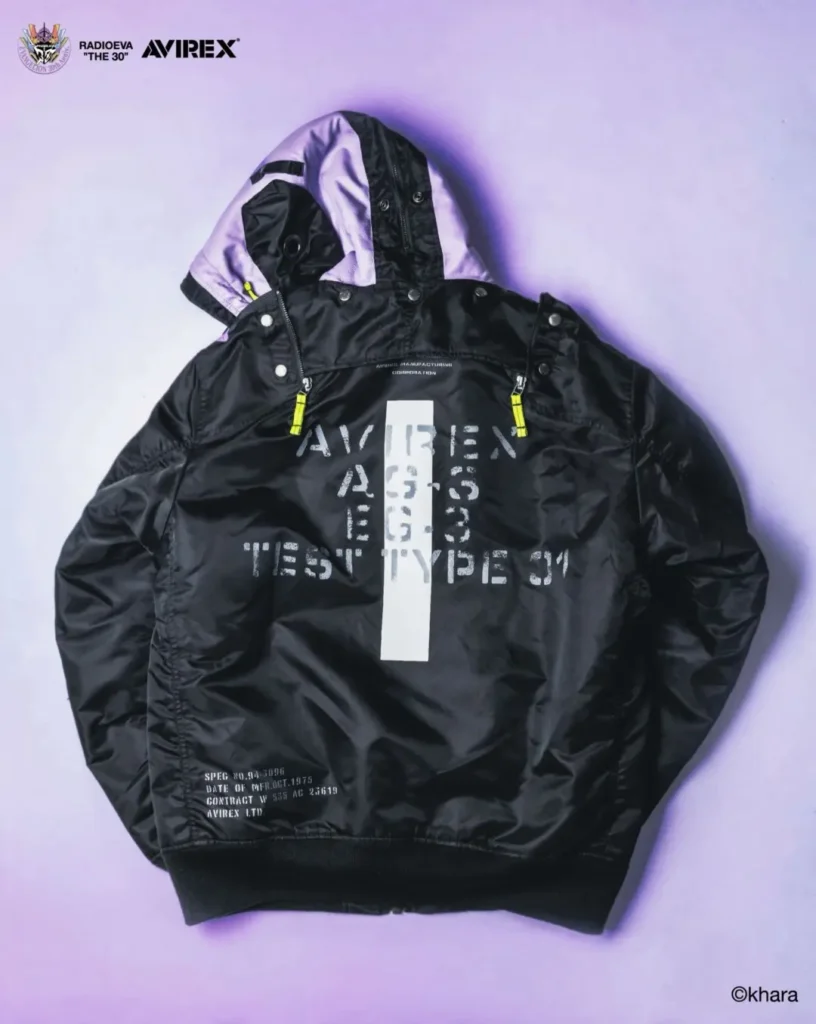 Black MA-1 jacket with purple hood lining, yellow zipper pulls and white distressed graphic, laid flat on a lavender