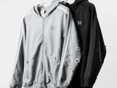 Gray and black distressed zip hoodies with butterfly logos hang from a metal clothing rack against a white background