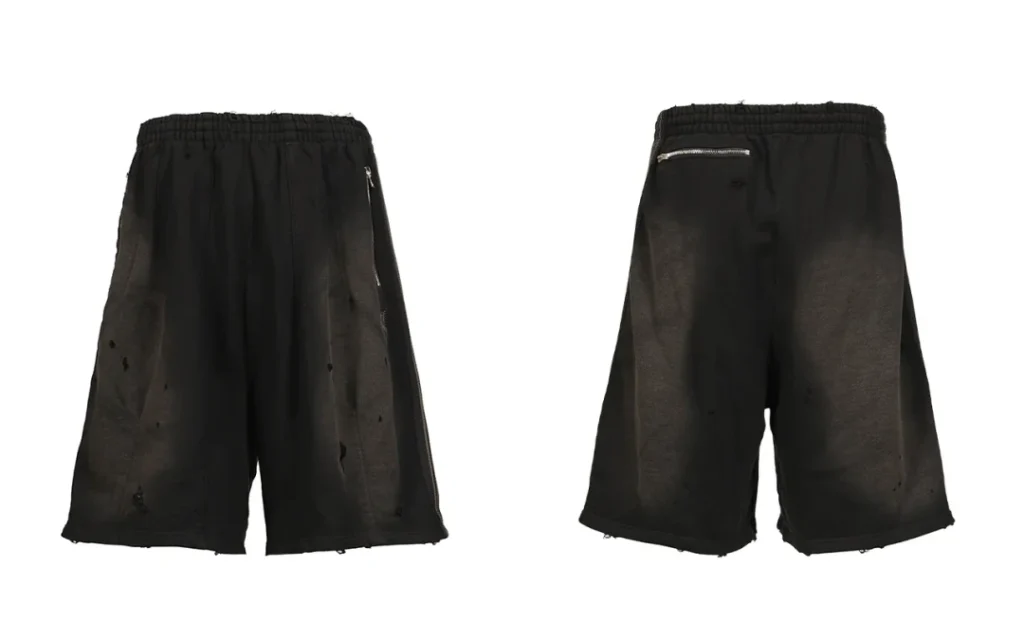 Front and back views of black distressed cotton jersey track shorts with elastic waist and zip pockets on a white background
