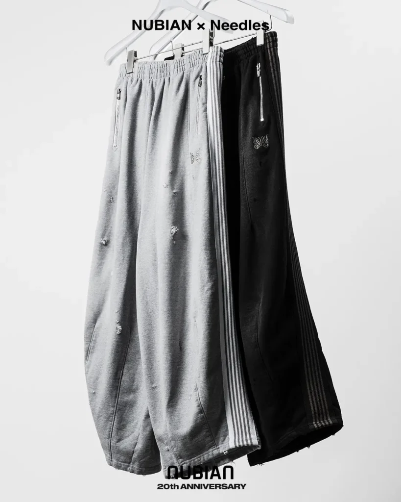 Gray and black distressed cotton track pants with striped side panels and zip pockets, hanging from white hangers against a