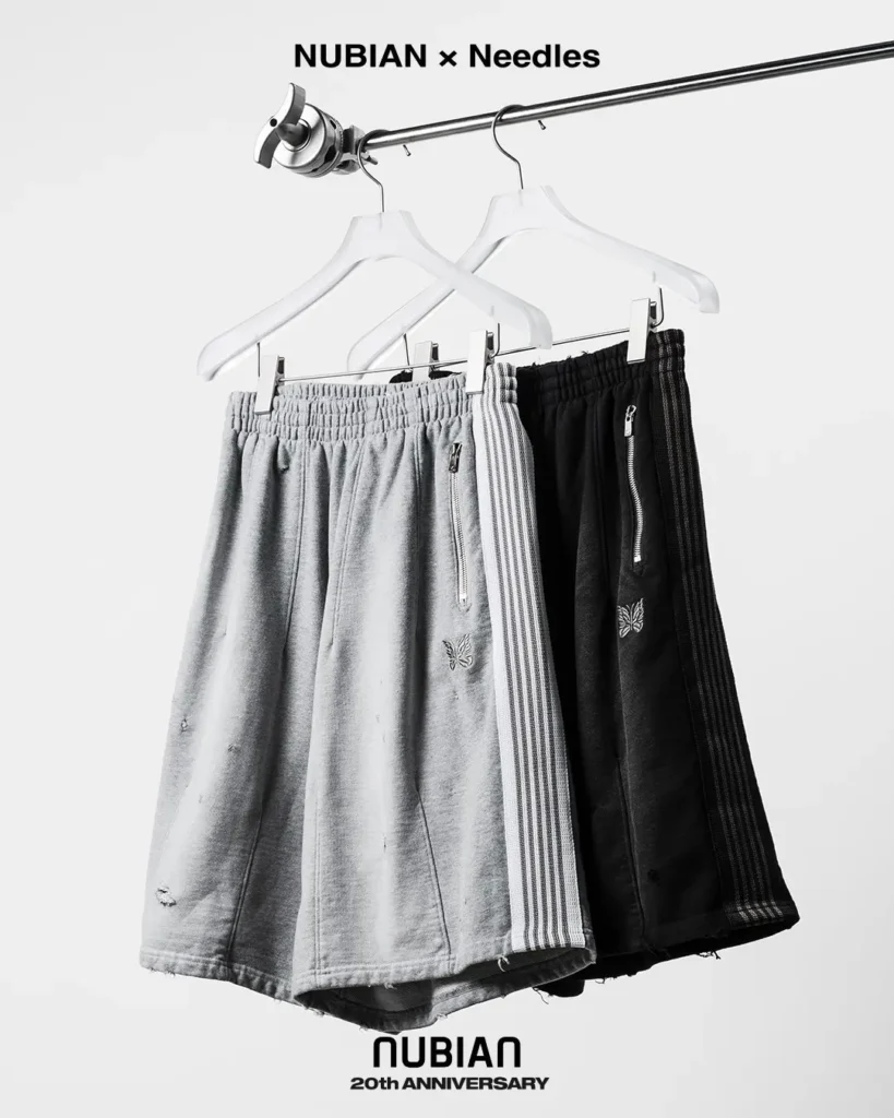 Gray and black distressed track shorts with striped side panels, zippers and butterfly logos hanging from white hangers