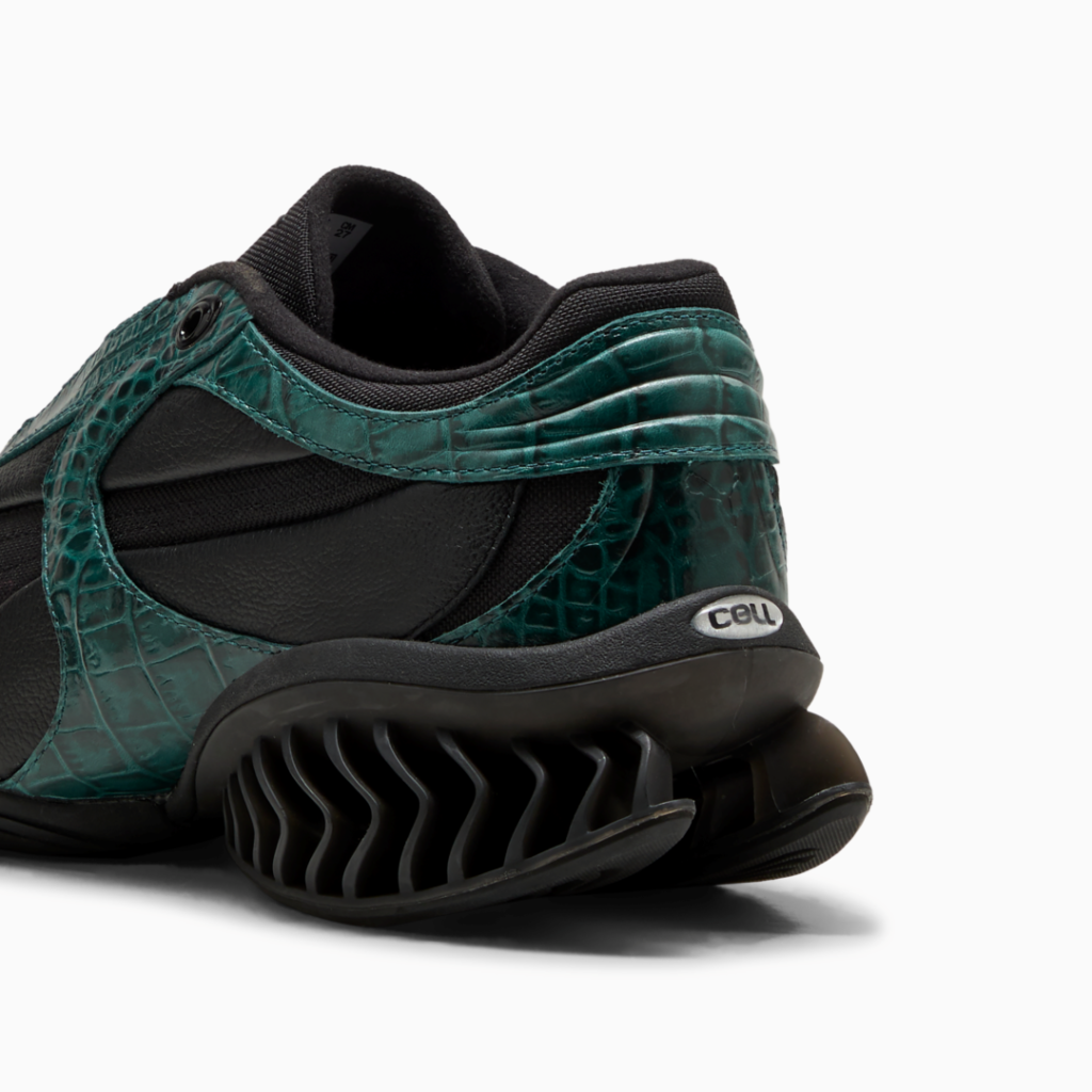 Close-up of a black sneaker with glossy teal crocodile-textured overlays and a ribbed black sole on a white background