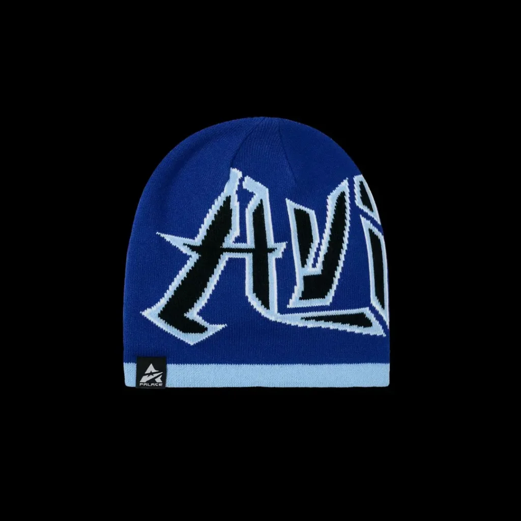 Blue knit beanie with oversized black-and-white graffiti-style lettering, light blue ribbed band and Palace logo on a black
