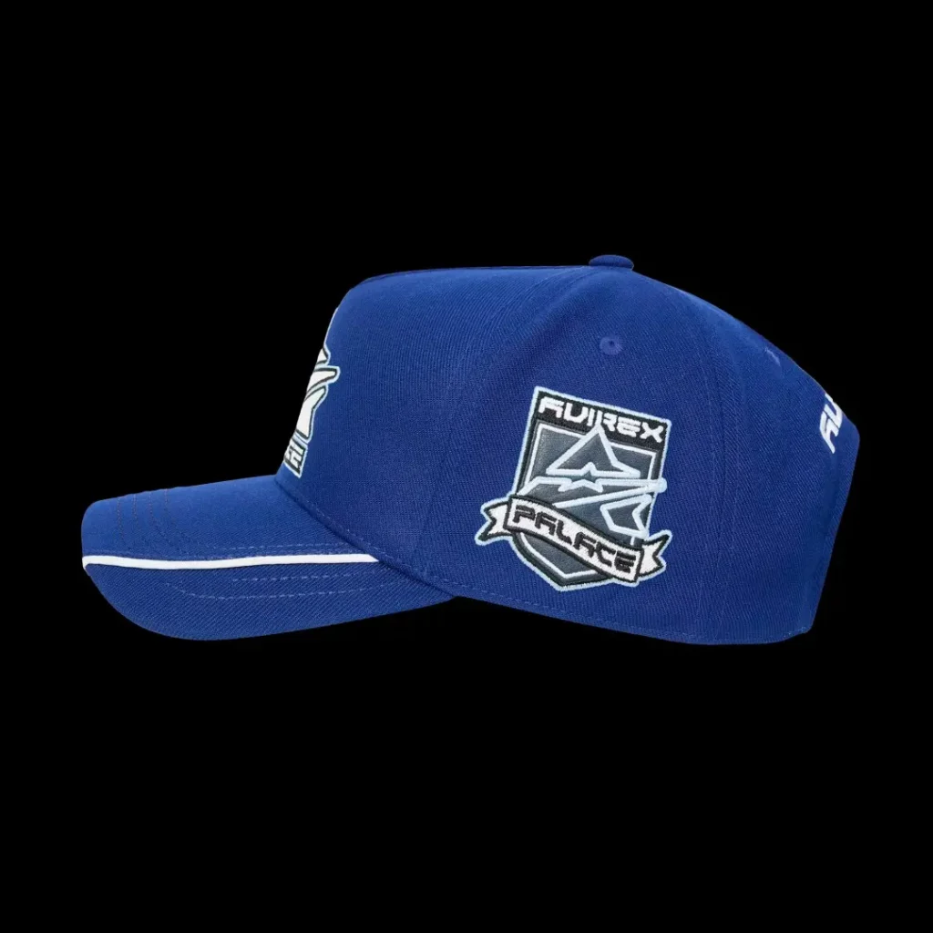 Blue baseball cap with white piping and a shield-shaped “PALACE” patch, shown against a black background
