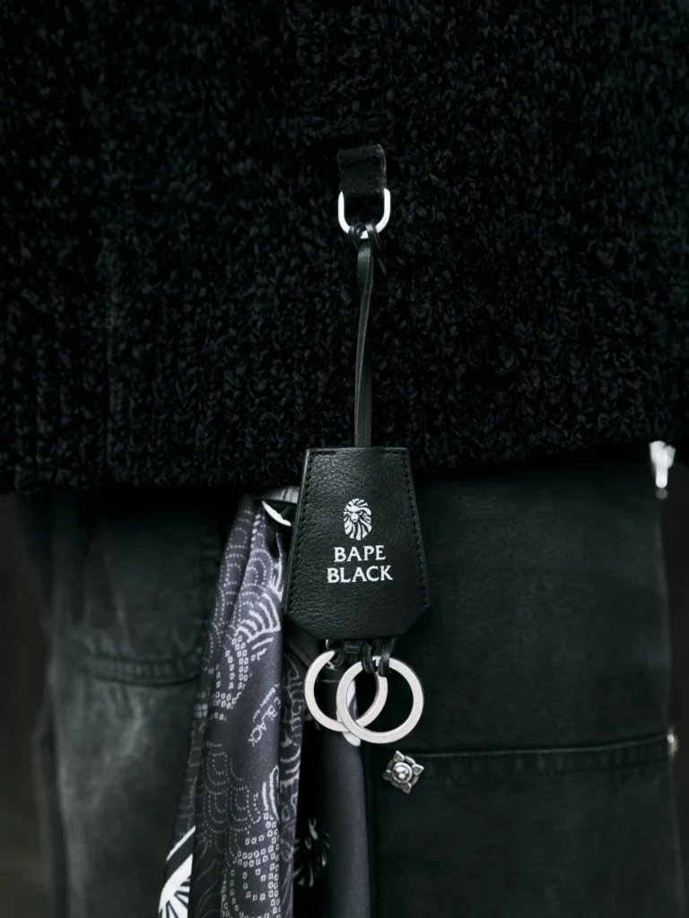 Black leather BAPE BLACK tag with metal rings and patterned scarf attached to a dark garment