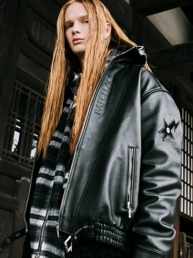 Long-haired person poses in a black leather jacket with a star sleeve patch and plaid lining before a dark building
