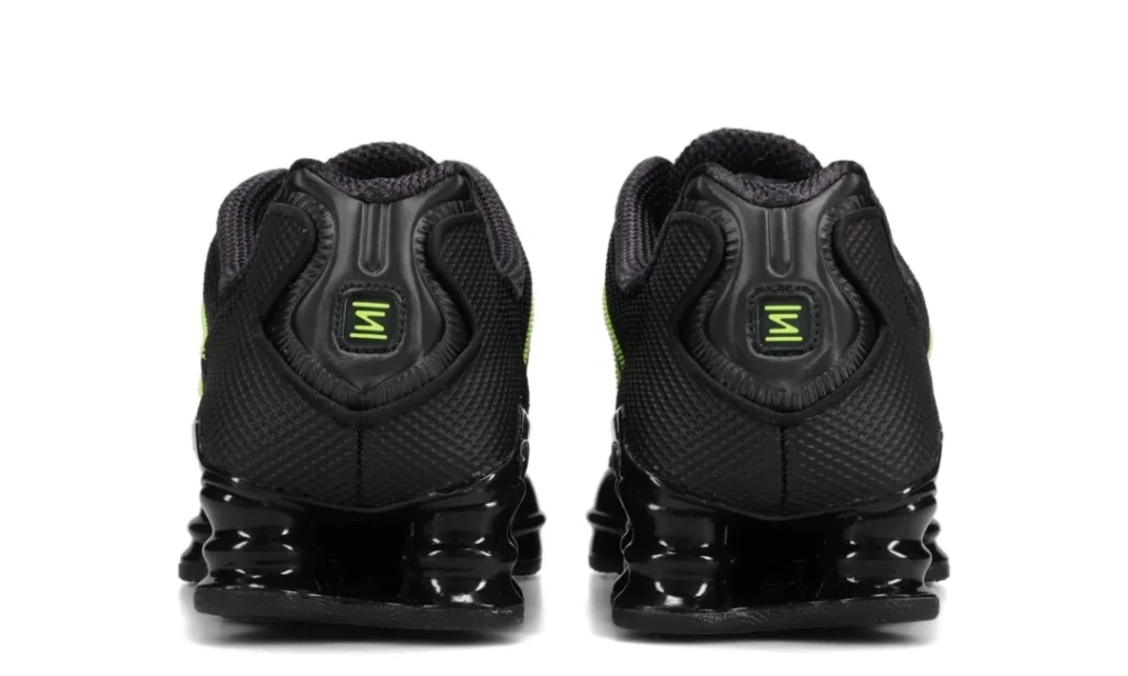 Rear view of a pair of black athletic shoes with glossy sculpted soles and small neon-green logos on the heels, on white
