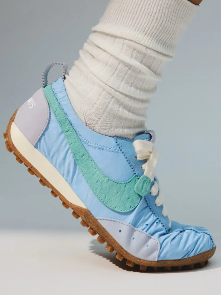 Close-up of a blue Nike shoe with a mint-green textured swoosh, white laces, gum sole, and ribbed white sock against pale