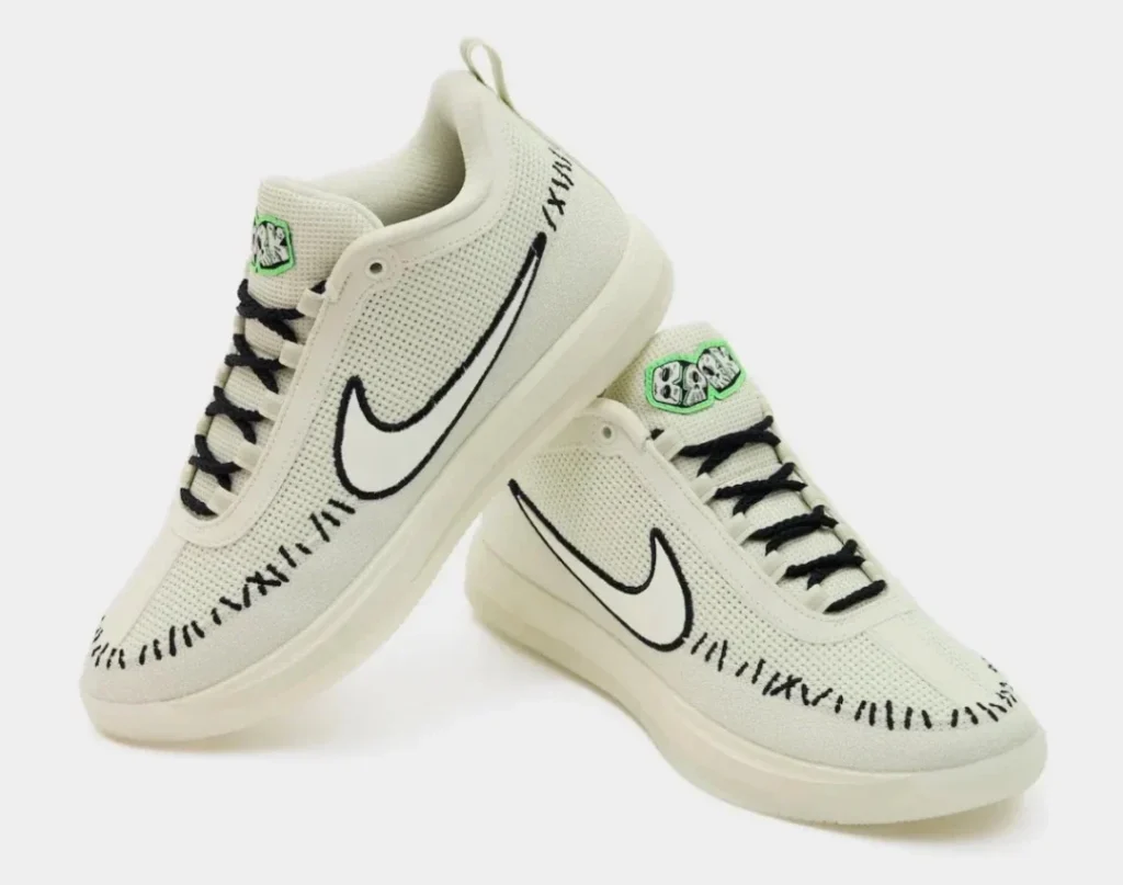 Pair of off-white Nike shoe with black Swooshes, laces and stitching, plus green-accented tongue labels on a white