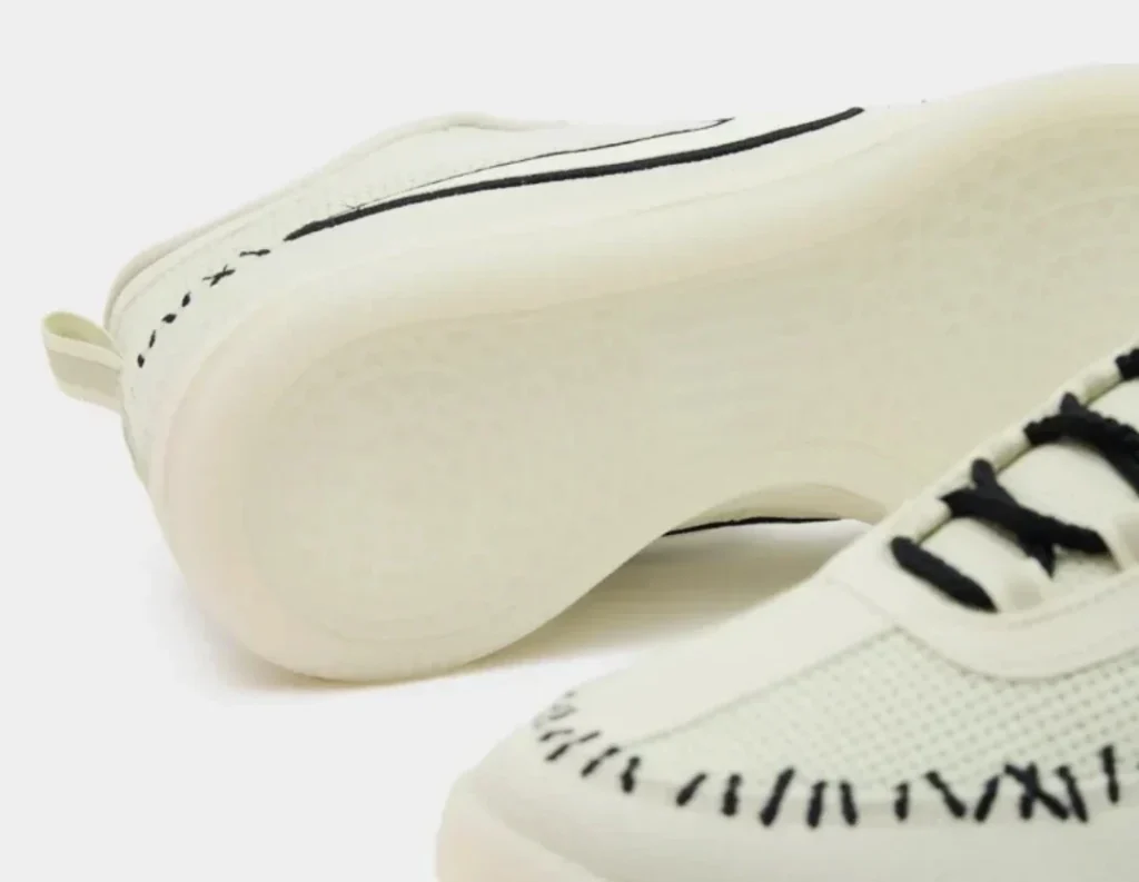 Close-up of cream sneakers with black laces and black stitched detailing on a white background