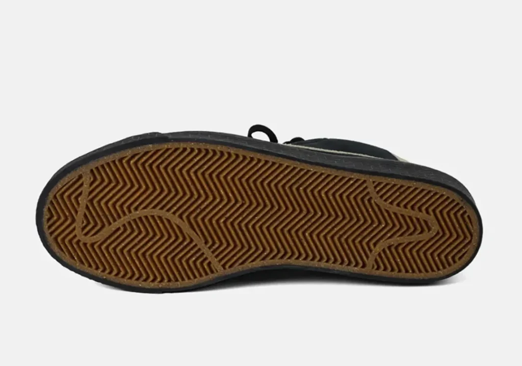 Underside of a black sneaker showing a brown rubber sole with dense herringbone tread and curved grooves