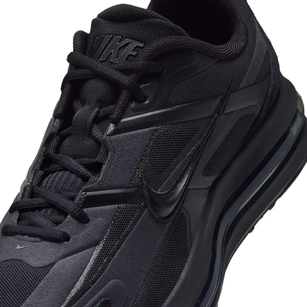 Close-up of a black Nike shoe with layered panels, mesh sections, laces, and a thick sculpted sole against white