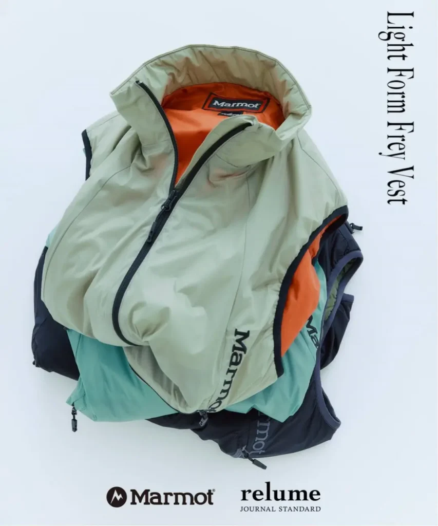 Pale green Marmot puffer vest with orange lining layered over teal and navy vests on a white background