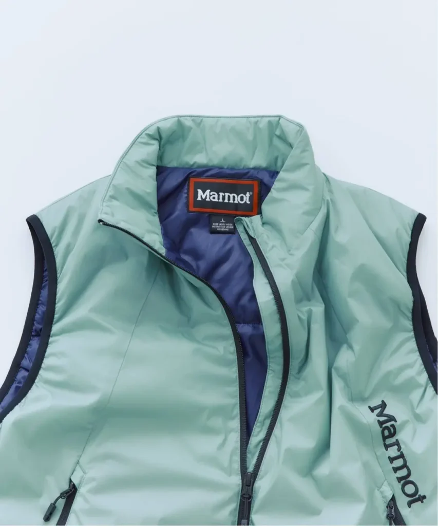 Mint green Marmot sleeveless jacket with navy lining, black trim and zippers, laid flat on a pale background