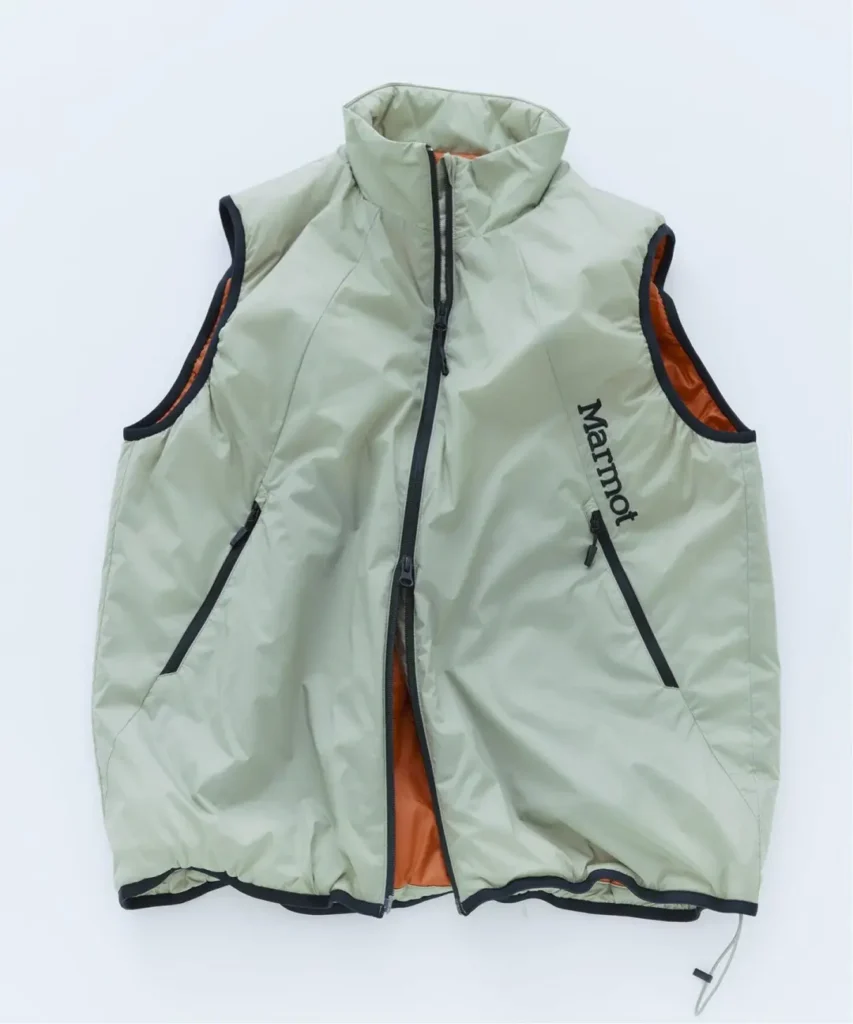 Light green Marmot insulated vest with orange lining, black trim, zip pockets and high collar, laid flat on white background