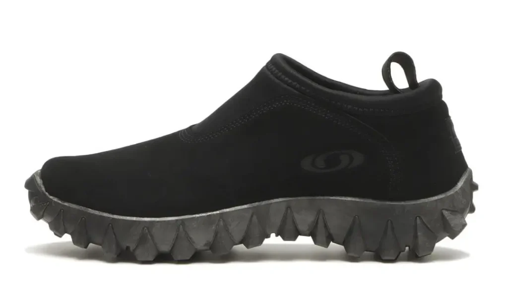 Black slip-on shoe with a looped heel tab and thick gray sole featuring deep triangular treads, shown in profile on white