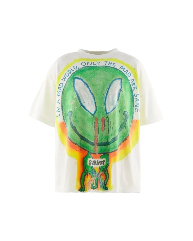 White T-shirt with a hand-painted green alien face, orange and yellow accents, and “Saint” text on a white background