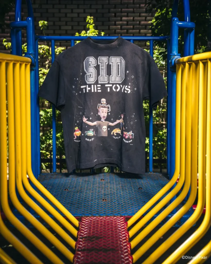 Black graphic T-shirt reading “SID THE TOYS” displayed on blue and yellow playground equipment