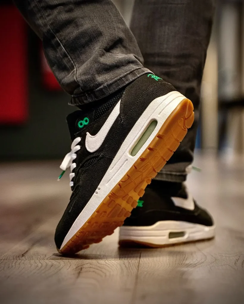 Close-up of black-and-white Nike sneakers with gum soles, one lifted over a wooden floor, worn with gray jeans