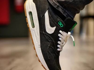 Close-up of a black Nike shoe with white swoosh and green accents, lifted above a wooden floor