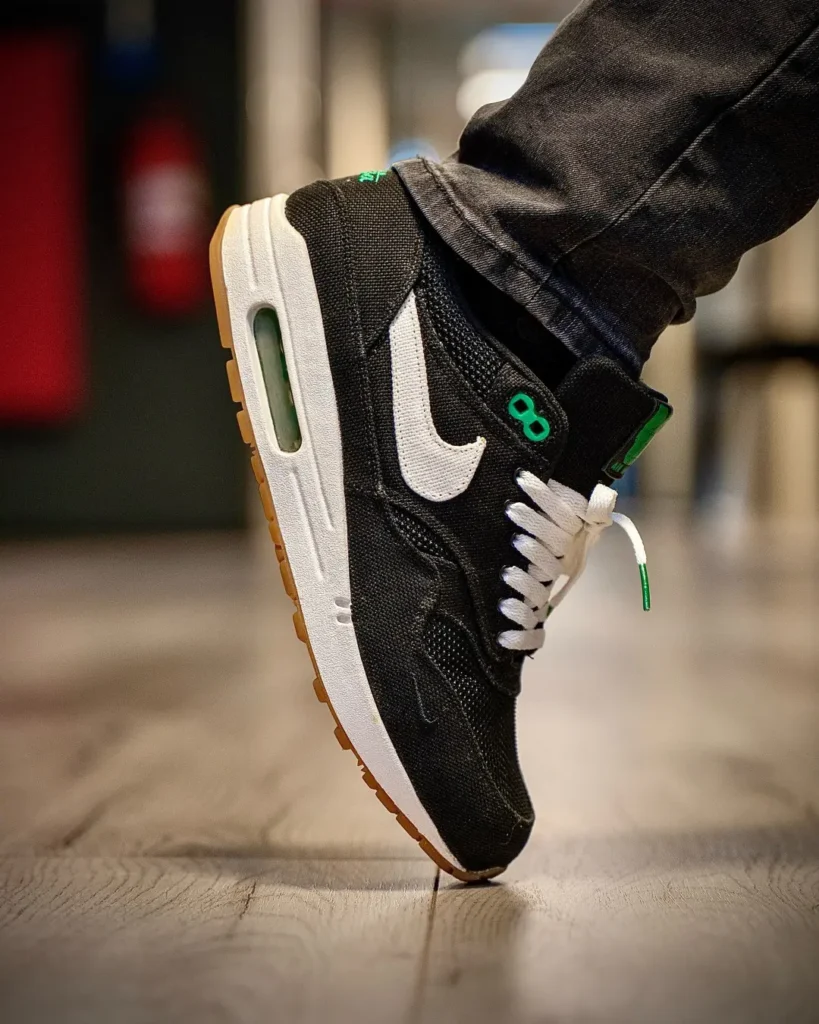 Close-up of a black Nike shoe with white swoosh and green accents, lifted above a wooden floor
