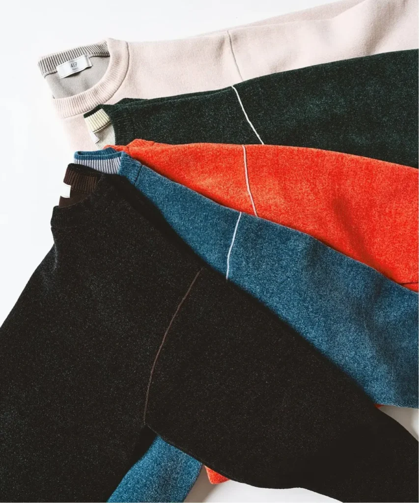 Stacked crewneck sweaters in black, blue, red, dark green and pale pink, with ribbed collars and contrasting seams on a