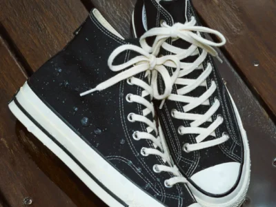 Pair of black canvas high-top sneakers with white laces and rubber toe caps on a wooden bench