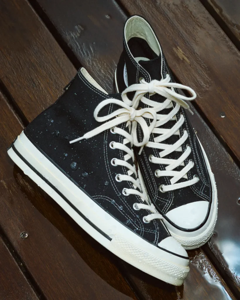 Pair of black canvas high-top sneakers with white laces and rubber toe caps on a wooden bench