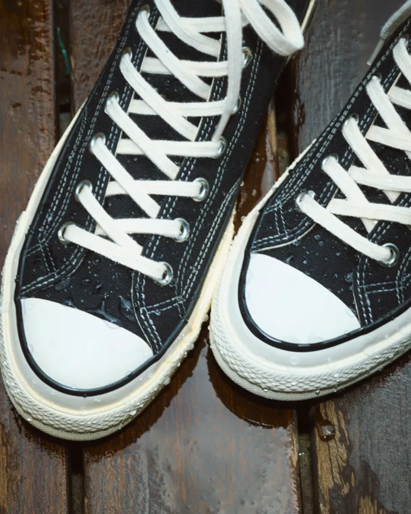 Black canvas sneakers with white laces and rubber soles on a wet wooden surface
