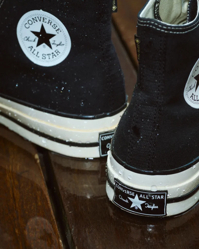 Close-up of black Converse All Star sneakers with white soles and water droplets on a dark wooden surface