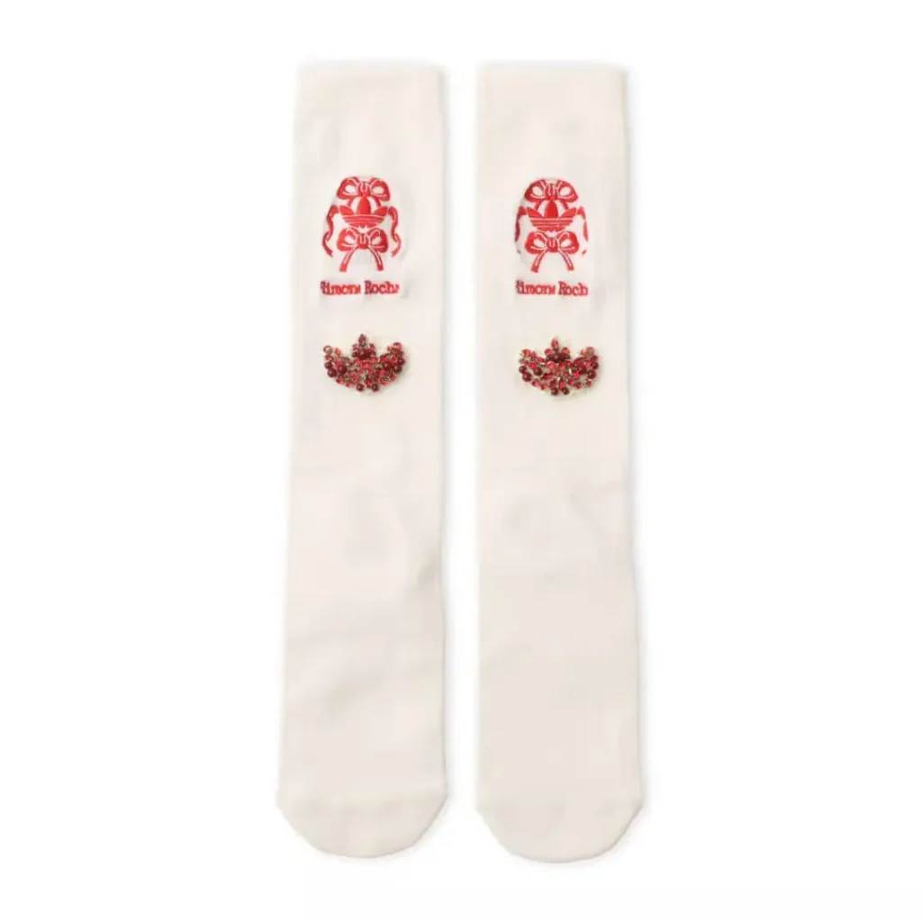 Pair of cream knee-high socks with red Simone Rocha logos and jeweled floral embellishments on a white background