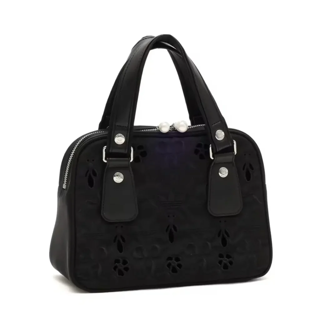 Black handbag with cutout floral pattern, twin handles, silver hardware and pearl zipper pulls on a white background