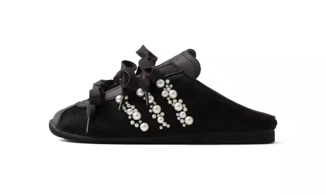 Black low-top shoe with straps and white pearl-like bead embellishments, shown in profile on a white background