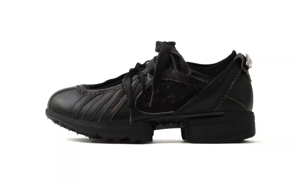 Black leather low-top sneaker with curved side panels, laces, rugged tread, and a thick segmented sole on white background