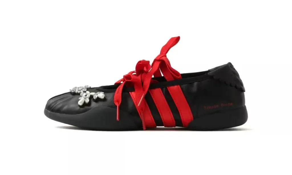 Black low-top sneaker with red ribbon laces, three red side stripes, and silver floral embellishment on a white background