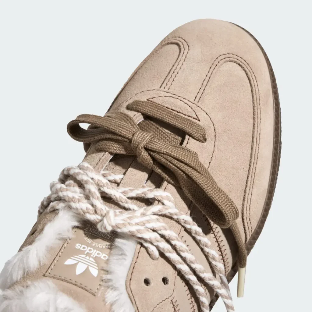 Close-up of a tan Adidas shoe with brown laces, white rope-like trim, stitched panels, and a textured rubber sole against