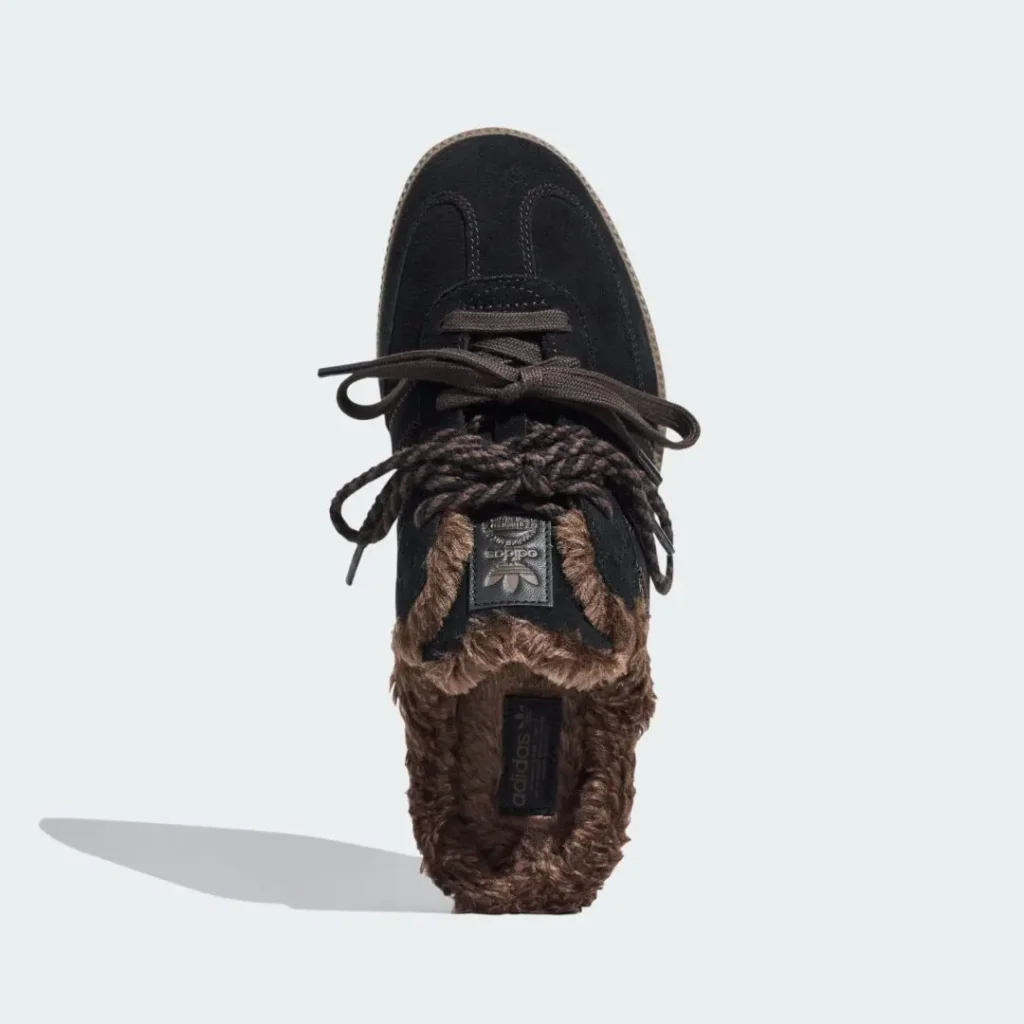 Top-down view of a black Adidas sneaker with brown fuzzy lining and loose dark laces on a pale background
