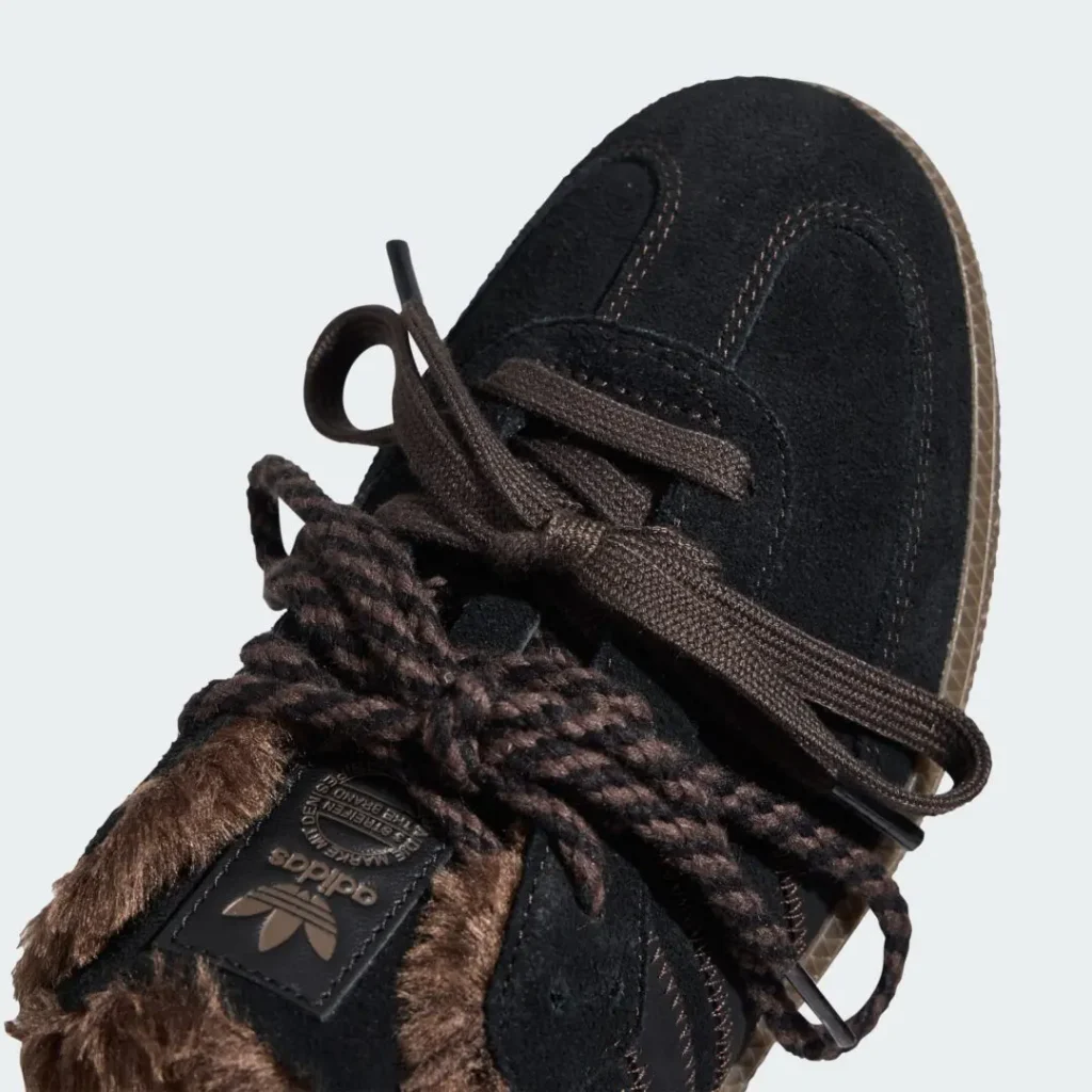 Close-up of a black Adidas sneaker with brown laces, fuzzy brown trim and a translucent textured sole against a pale