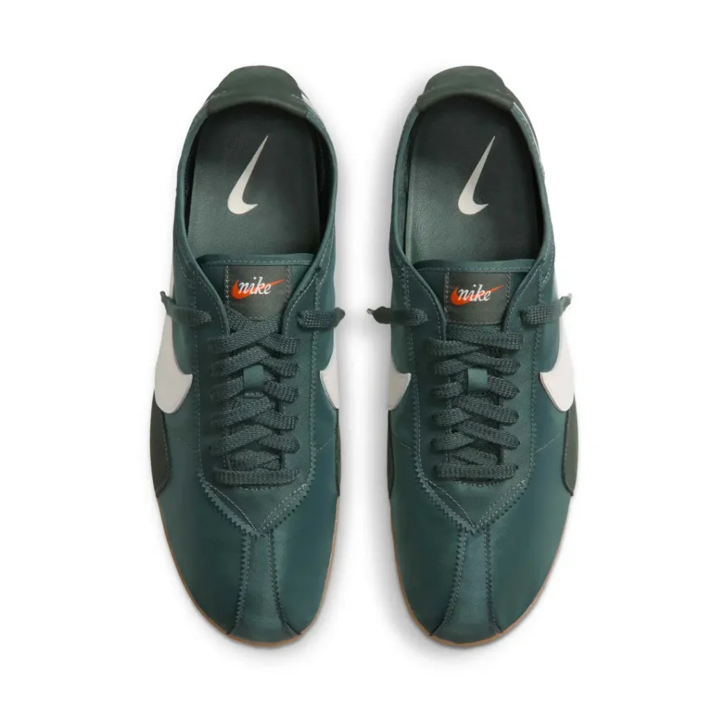 Top-down view of green Nike sneakers with white swooshes, dark laces, orange tongue labels, and gum soles on white background