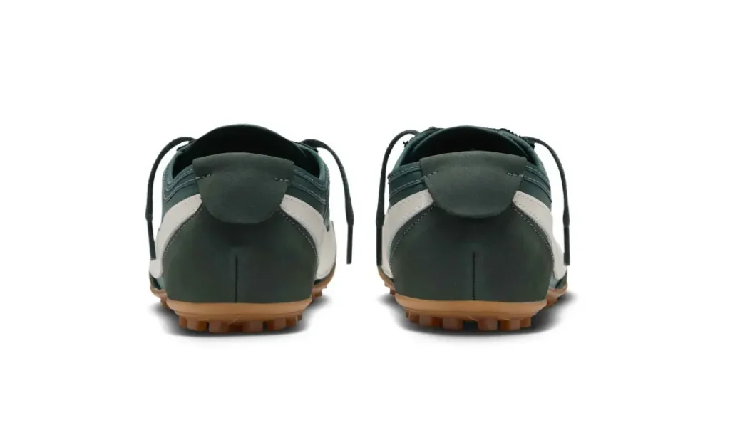 Rear view of a pair of dark green and cream sneakers with gum soles and loose black laces on a white background