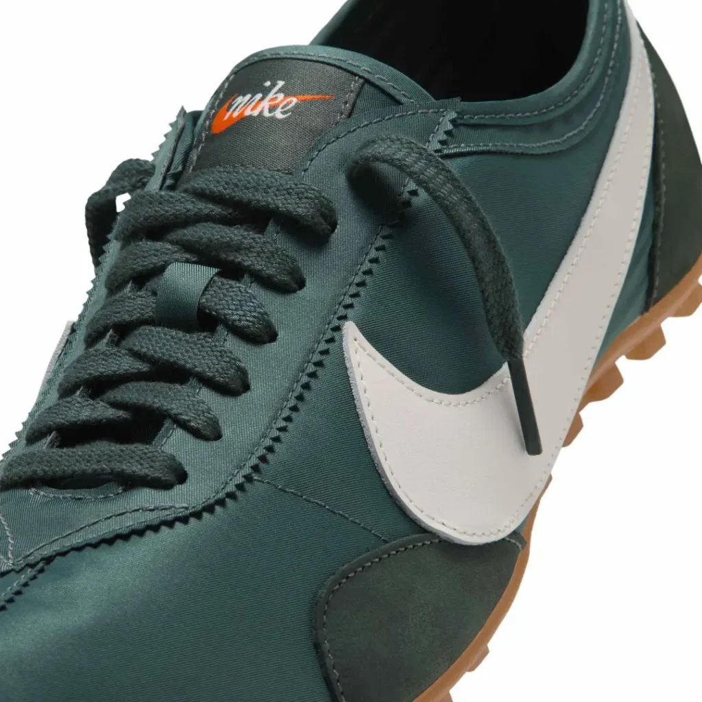 Close-up of a dark green Nike sneaker with black laces, white swoosh, orange tongue logo, and gum outsole against white
