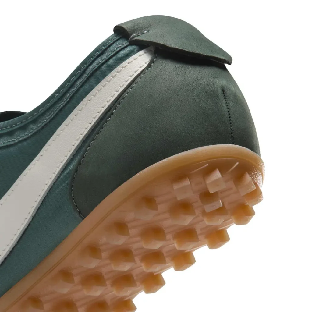 Close-up of a dark green shoe with a white side stripe and translucent gum sole against a white background