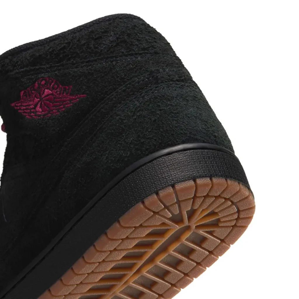 Close-up of a black textured shoe showing a burgundy embroider logo and gum rubber tread sole against white background