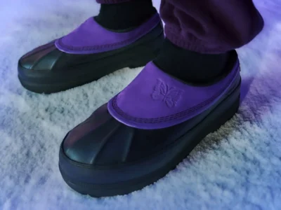 Close-up of purple-and-black waterproof boots with embossed butterfly logos, worn with purple pants on snowy ground