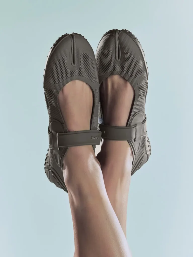 Close-up of crossed legs in gray mesh sandals with thick straps and textured rubber soles against a pale blue background
