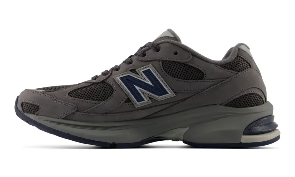 Gray New Balance sneaker with navy logo, mesh panels, layered leather upper, and chunky sculpted sole on a white background