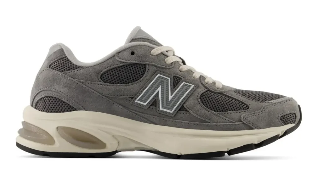 Gray New Balance sneaker with mesh panels, suede overlays, cream laces, and an off-white sculpted sole on white background