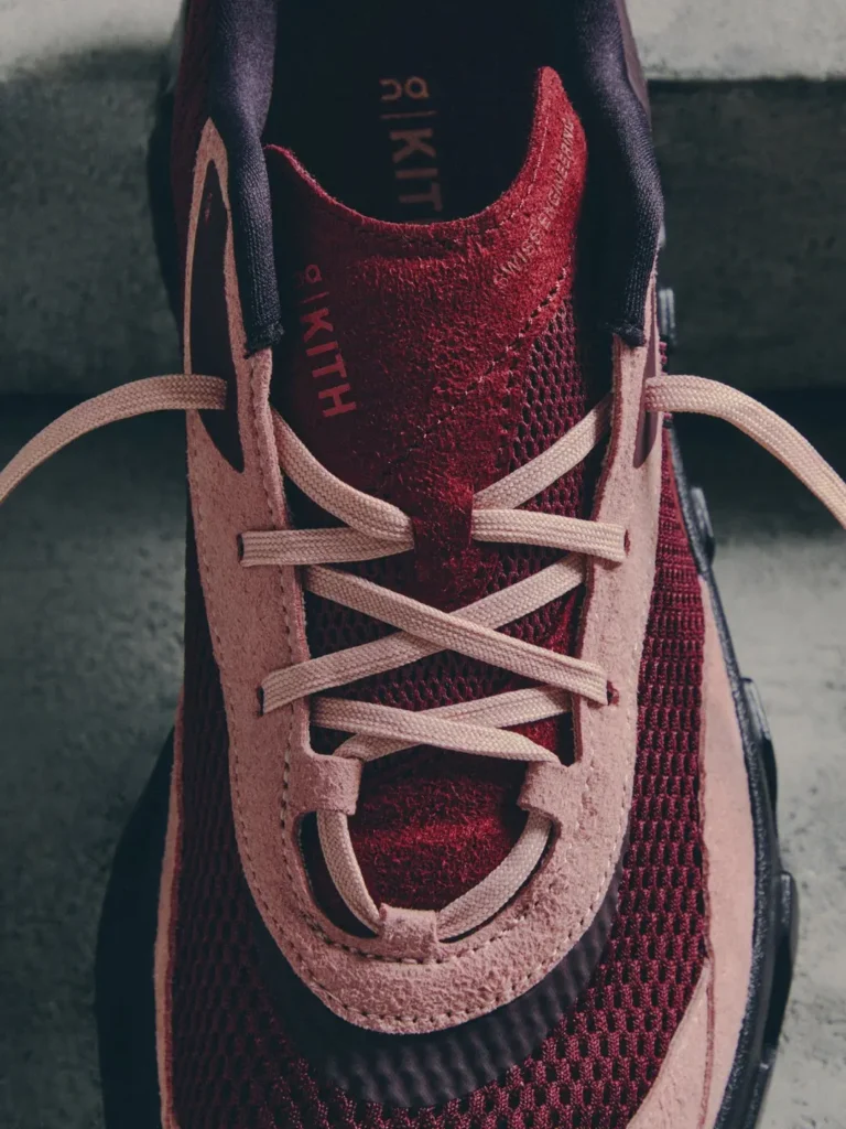 Close-up of a burgundy mesh sneaker with pale pink leather panels and crisscrossed laces on concrete