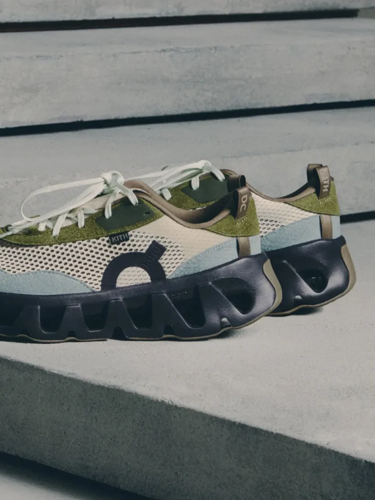Pair of green, cream and black athletic sneakers with white laces and oversized sculpted soles on concrete steps