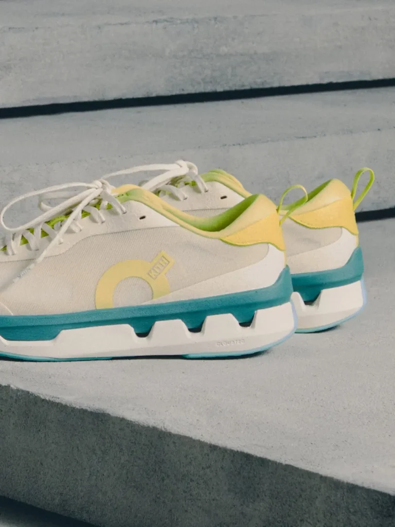Pair of white sneakers with lime-green and yellow accents, turquoise soles, and white laces on concrete steps